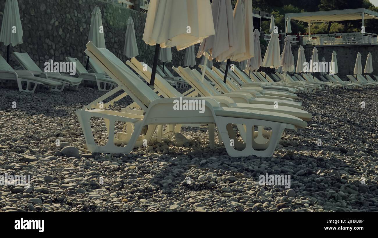 Chaise-longues in plastica bianca sulla spiaggia di ciottoli Foto Stock