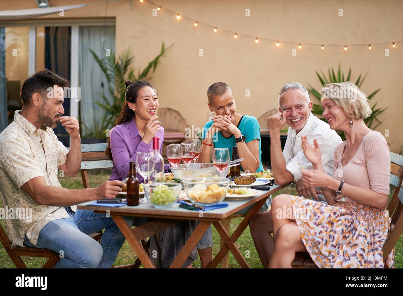 Gruppo di amici felici che si divertono bevendo vino rosso al barbecue picnic giardino party. Persone di mezza età che mangiano un pasto gustoso nel cortile. Foto Stock