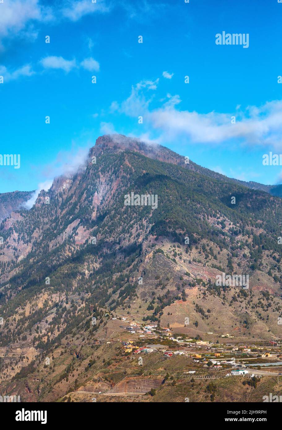 Bel paesaggio di cima di montagna vicino a una piccola città o villaggio. Vista panoramica e tranquilla di un picco con un cielo blu nuvoloso su sfondo in una giornata estiva Foto Stock