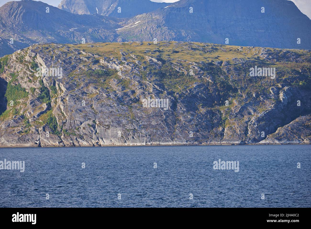 Il paesaggio di un mare calmo vicino a una montagna rocciosa. Una serie di verdi colline montane presso un grande lago in Norvegia. Oceano pacifico in una costa selvaggia di Foto Stock