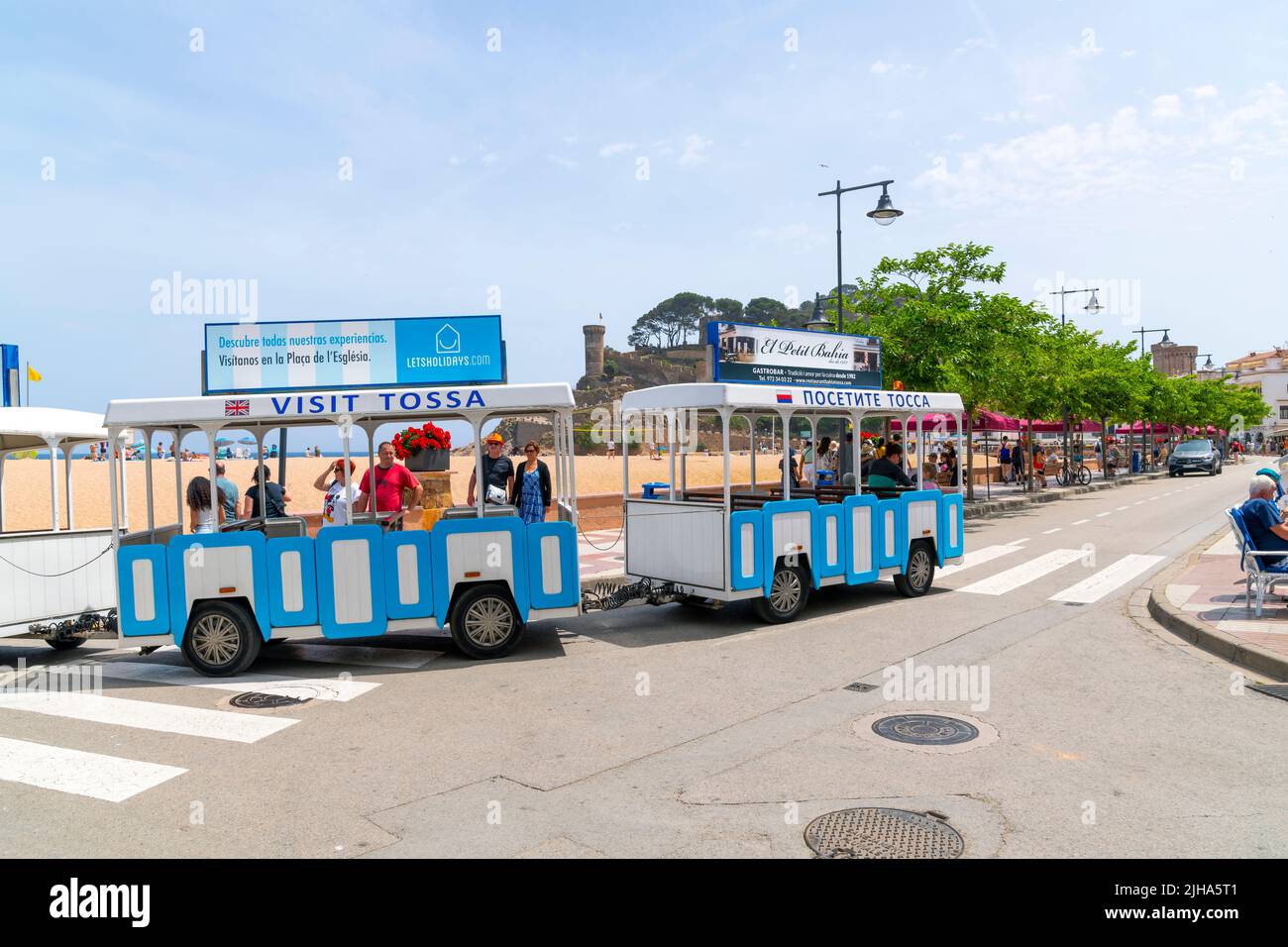 Il treno turistico corre lungo la spiaggia sabbiosa e la città vecchia della Costa Brava, località balneare mediterranea di Tossa de Mar, Spagna. Foto Stock