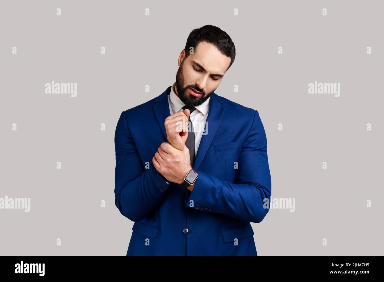 Ritratto di uomo d'affari in piedi con grimace di dolore, massaggiando il polso irritato, soffrendo la ferita della mano o la pioggia, indossando il vestito ufficiale di stile. Studio interno girato isolato su sfondo grigio. Foto Stock