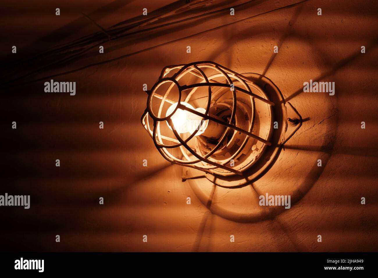 Lampada incandescente. Una vecchia lampadina elettrica con una griglia di metallo sulla parete Foto Stock