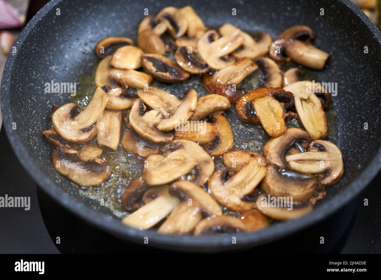 Affettati i funghi in una padella sul piano cottura a induzione della cucina domestica Foto Stock