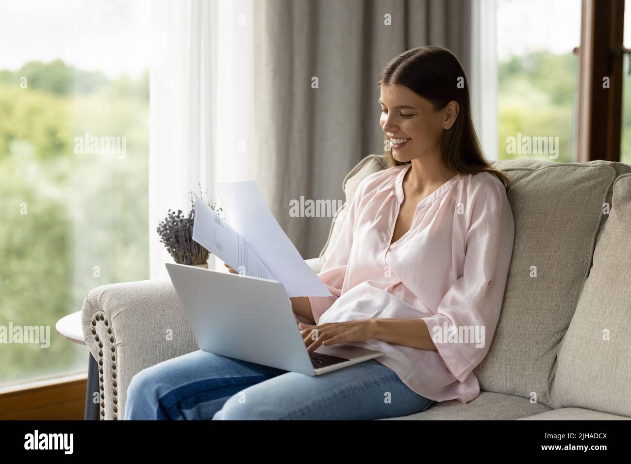 Donna attraente smistamento fuori carte sedersi sul divano uso laptop Foto Stock