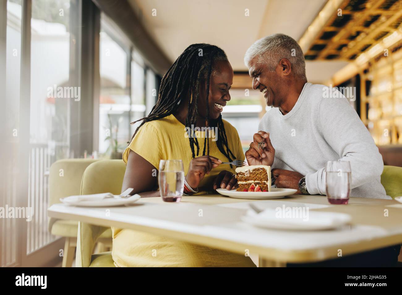 Coppia matura felice ridendo allegro mentre condividendo una deliziosa torta in un caffè. Spensierate la coppia anziana che si è recata bene in un ristorante. Maturo co Foto Stock