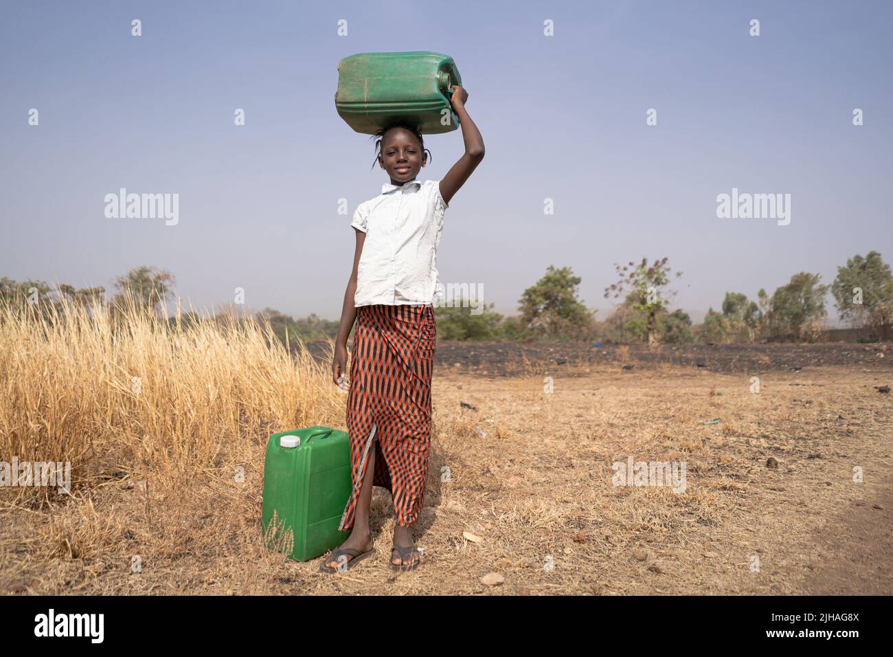 Ragazza africana con canister verdi in un paesaggio savana, che simboleggia la mancanza di infrastrutture idriche nei paesi in via di sviluppo Foto Stock