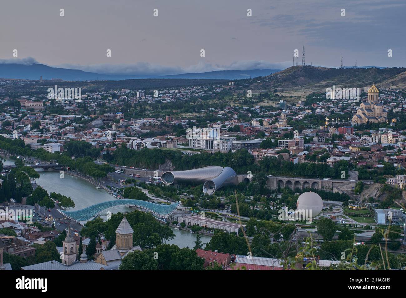 Tbilisi, Georgia tramonto Vista panoramica dalla cima della fortezza di Narikala che mostra il ponte della pace, Rike Park, fiume Kura e Cattedrale della Santissima Trinità Foto Stock