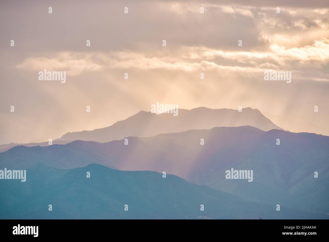 Una carta da parati estetica con morbide nuvole nel cielo con raggi solari che cadono sulle montagne Foto Stock
