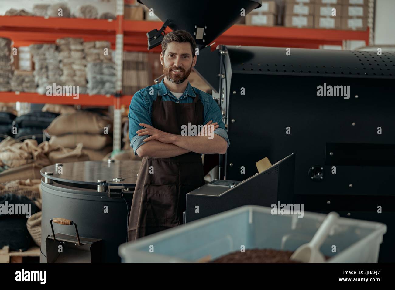 Il proprietario di affari sorridente sta in piedi sullo sfondo della macchina di tostatura del caffè Foto Stock