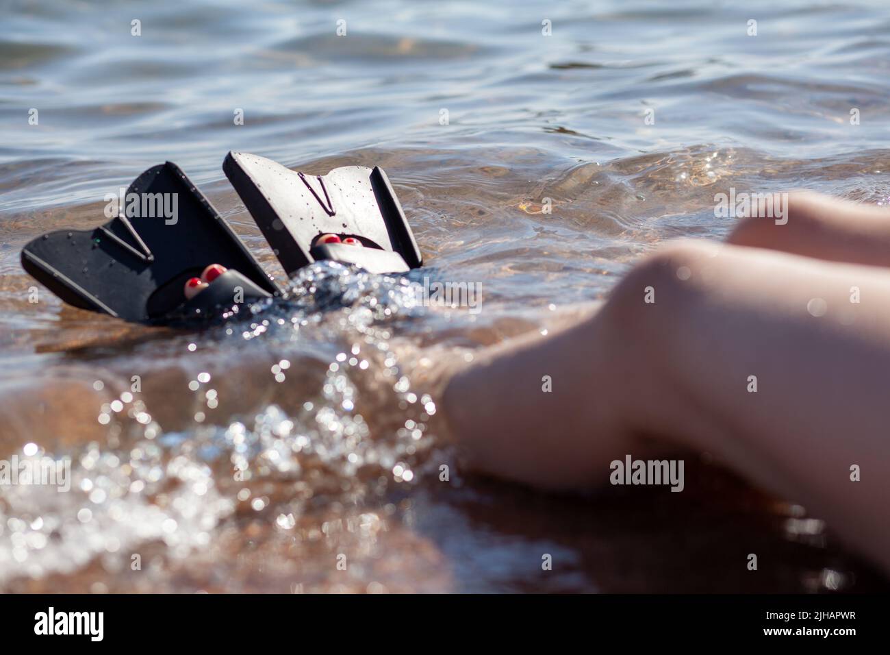 Una donna in pinne nere spruzza vicino alla riva. Le pinne sporgono dall'acqua. Attrezzature per il nuoto. Vacanze estive, divertimento, esplorare il mondo del mare ecc Foto Stock