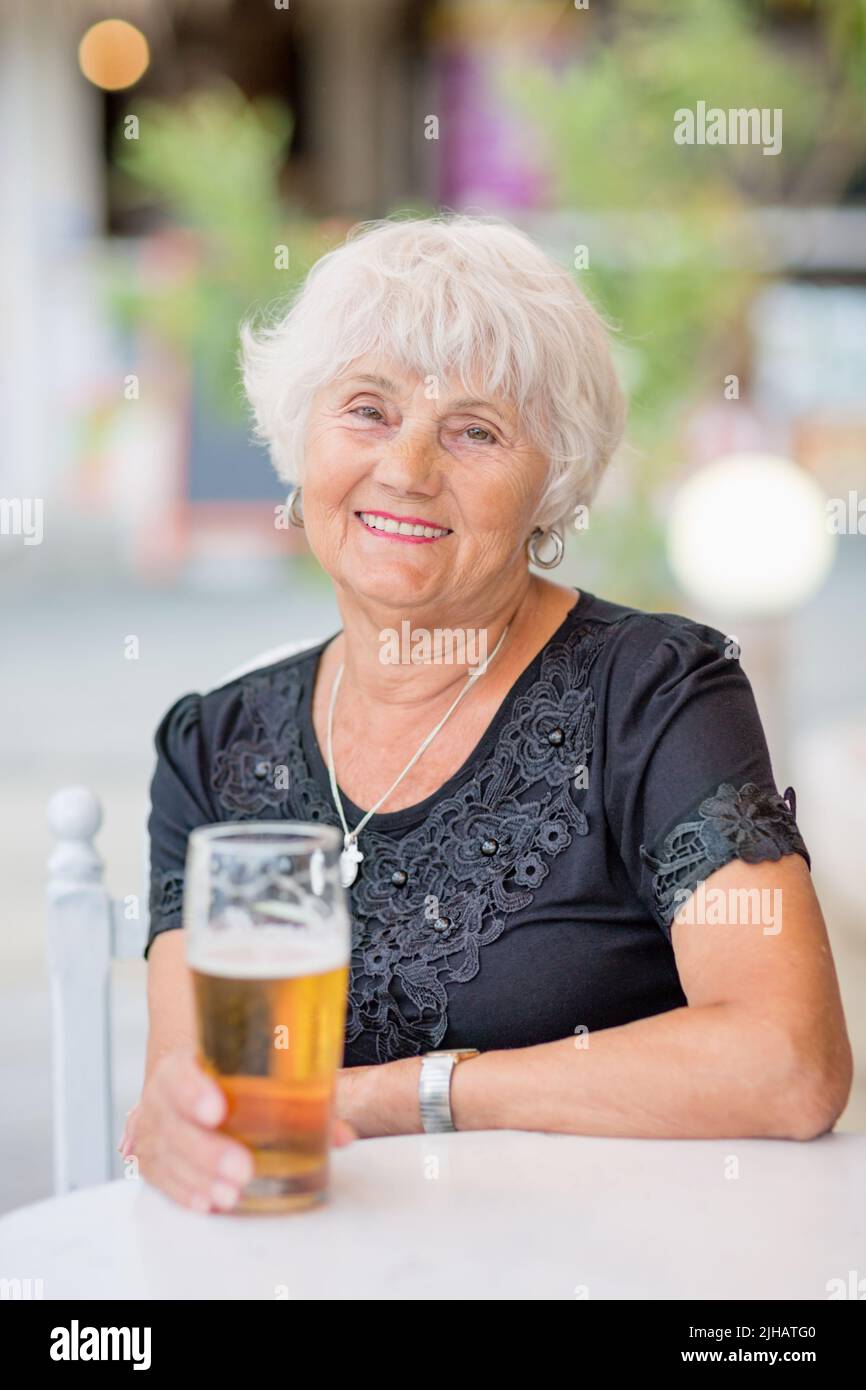 Donna matura seduta a un tavolo in un bar estivo e bere birra Foto Stock
