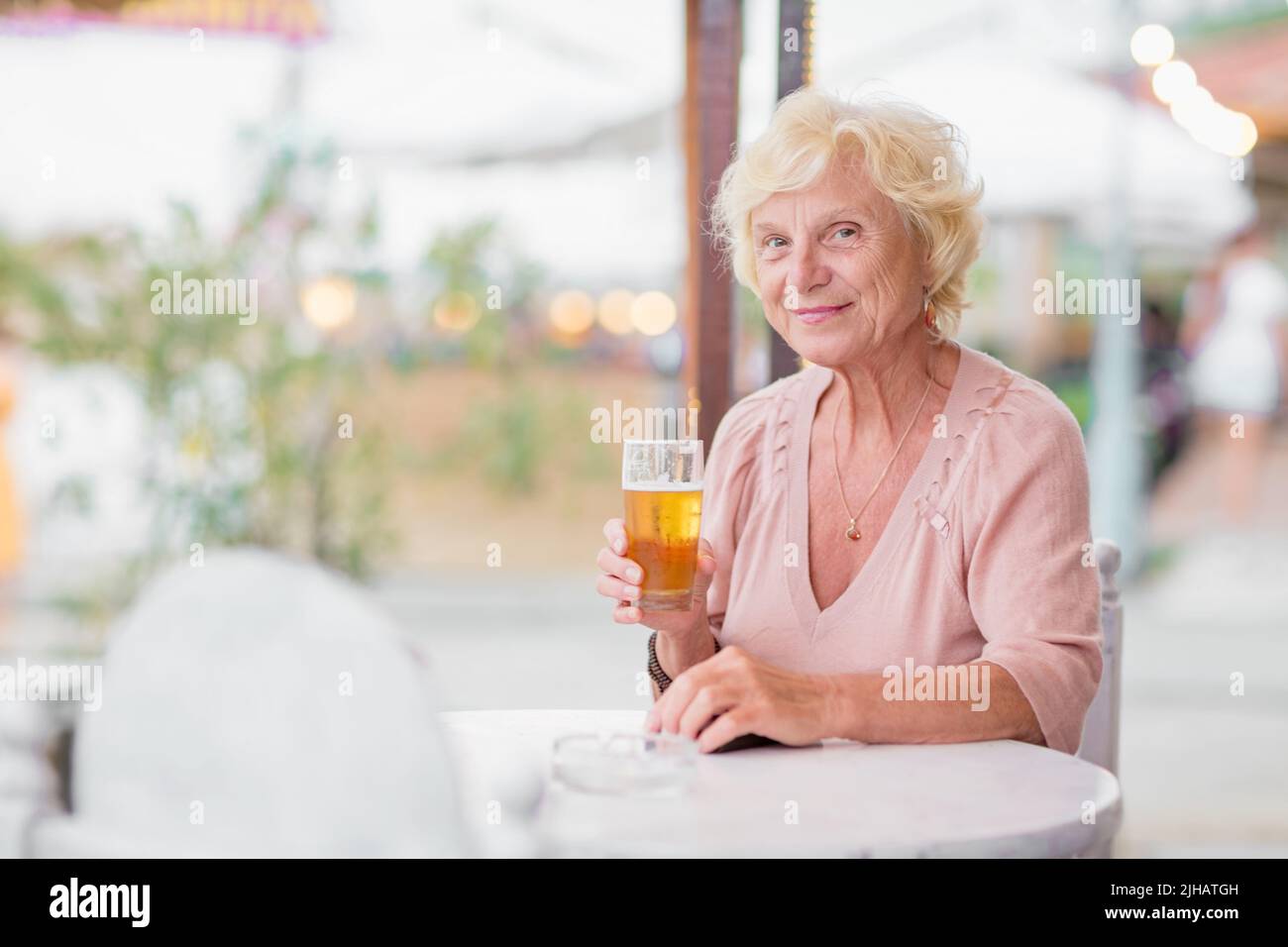 Donna matura seduta a un tavolo in un bar estivo e bere birra Foto Stock