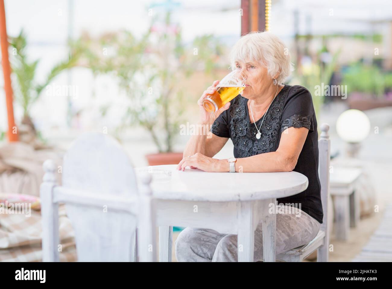 Donna matura seduta a un tavolo in un bar estivo e bere birra Foto Stock