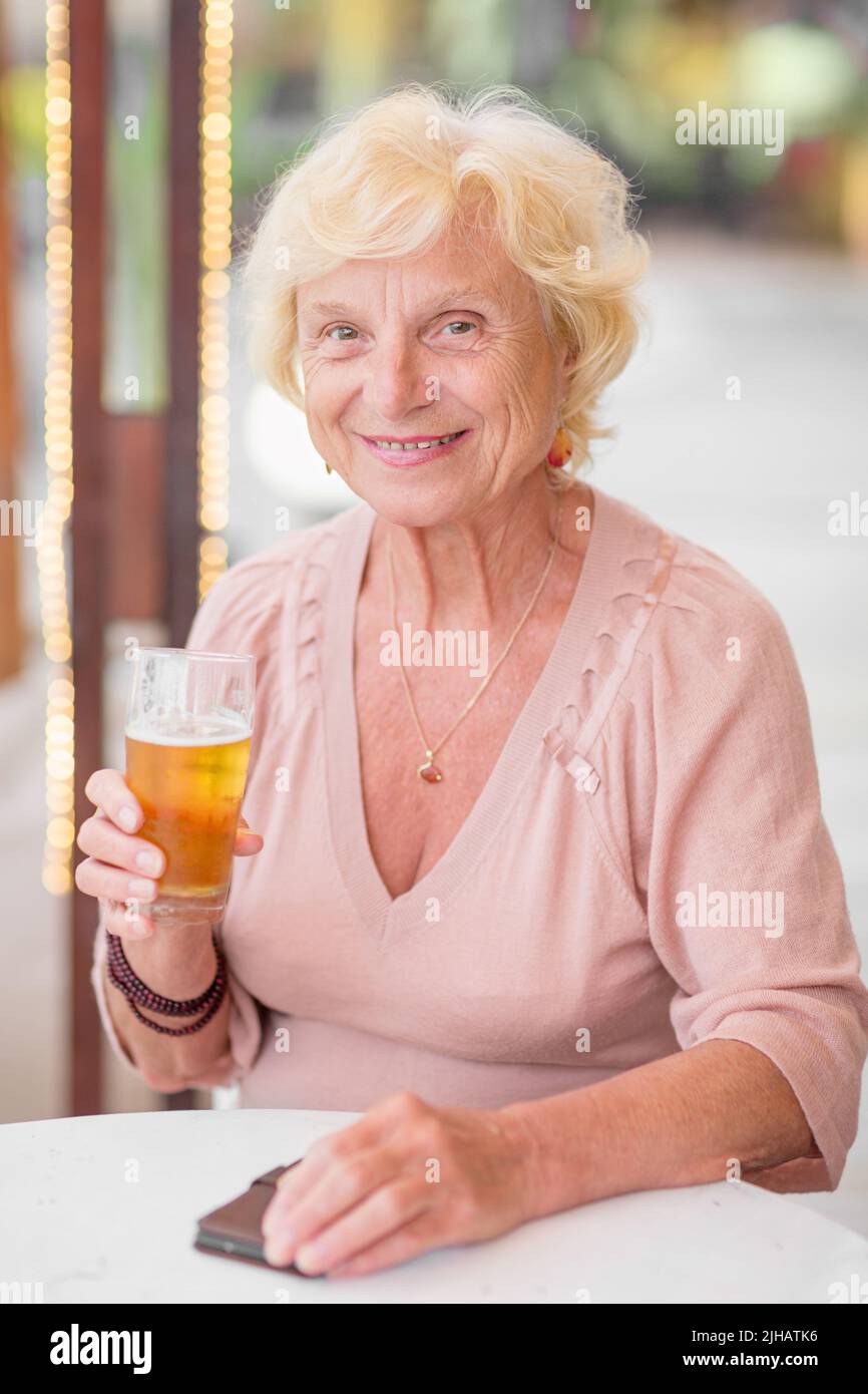 Donna matura seduta a un tavolo in un bar estivo e bere birra Foto Stock
