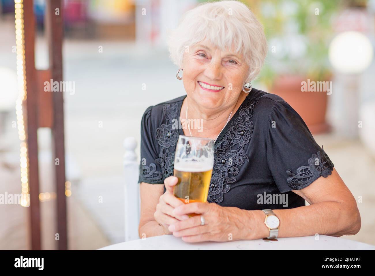 Donna matura seduta a un tavolo in un bar estivo e bere birra Foto Stock
