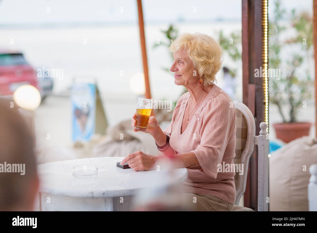Donna matura seduta a un tavolo in un bar estivo e bere birra Foto Stock
