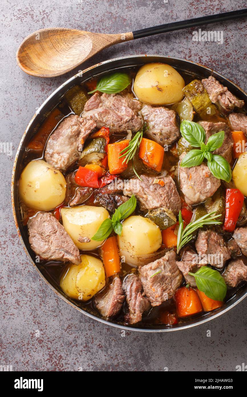 Deliziosa peka croata cucinata a base di carne di vitello con verdure di stagione ed erbe in primo piano sul tavolo. Vista dall'alto verticale Foto Stock