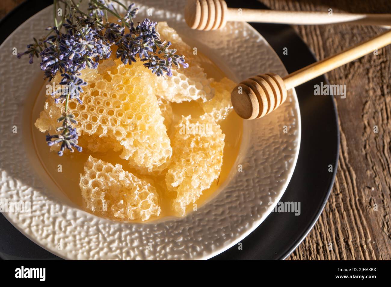 Miele e nido d'ape su un piatto bianco. Cibo dolce in una ciotola sul tavolo. Un prodotto dell'apicoltura. Fiore di lavanda. Foto Stock