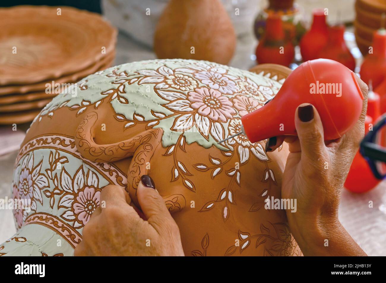 Rodi, Grecia - Maggio 2022: Vista ravvicinata di un artista di ceramica che usa la vernice liquida colorata per riempire un modello intricato su un vaso grande Foto Stock