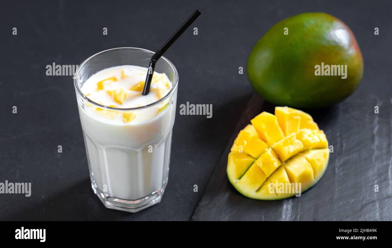 Bevanda al latte su sfondo nero con mango. Un classico milkshake di mango - Lassi. Una bevanda tradizionale in India dal calore Foto Stock