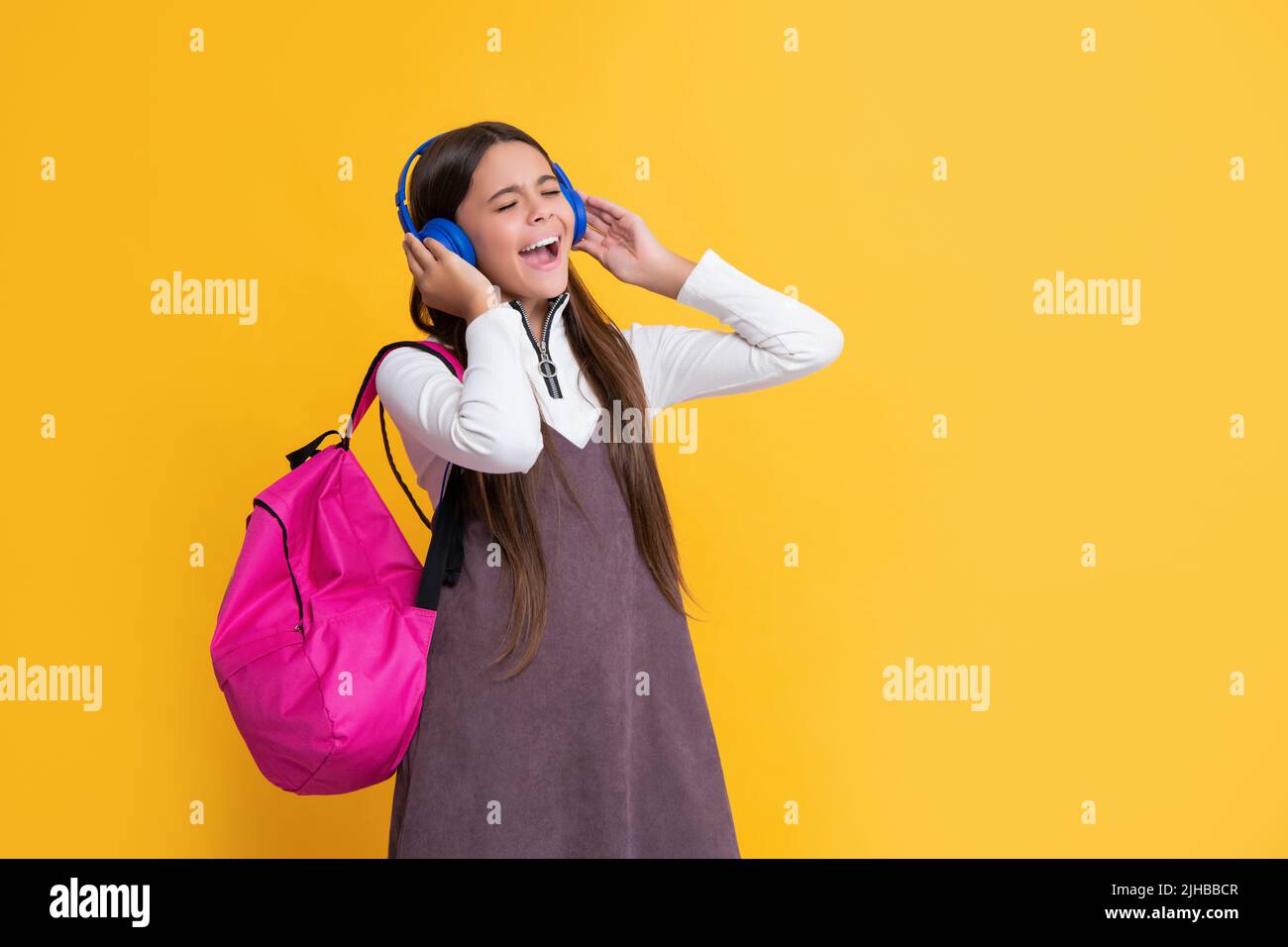 il bambino stupito in cuffie con zaino scuola su sfondo giallo Foto Stock