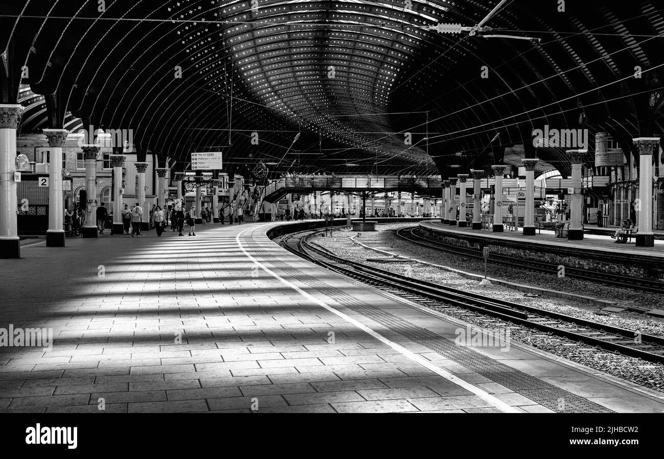 La luce del sole di un lucernario cade su una piattaforma della stazione ferroviaria che fa un modello a strisce. I passeggeri si riuniscono sulla piattaforma. Foto Stock