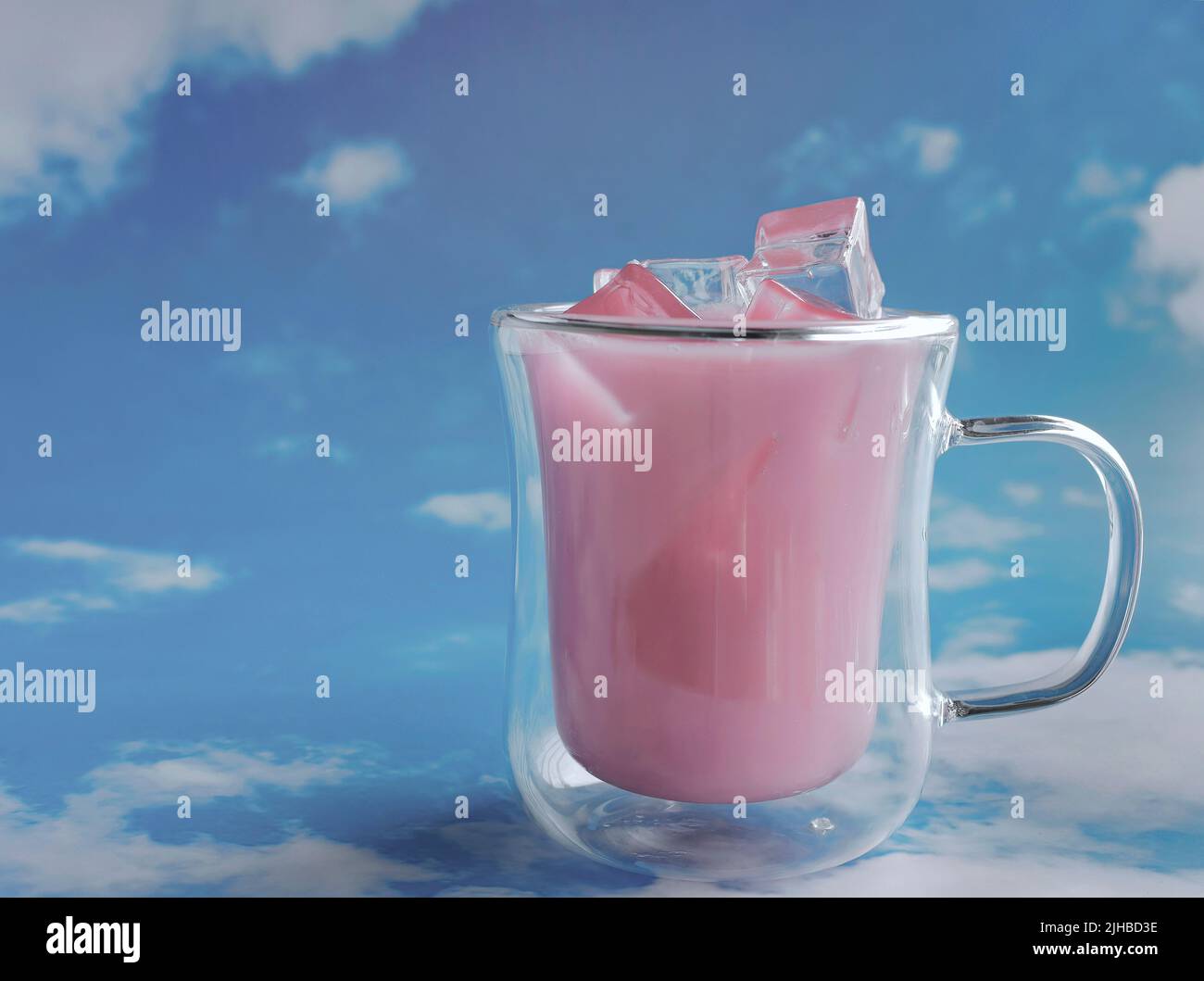 Primo piano tazza di vetro doppia riempita di colore rosa pastello bevanda con sfondo blu cielo, tema pastello Foto Stock