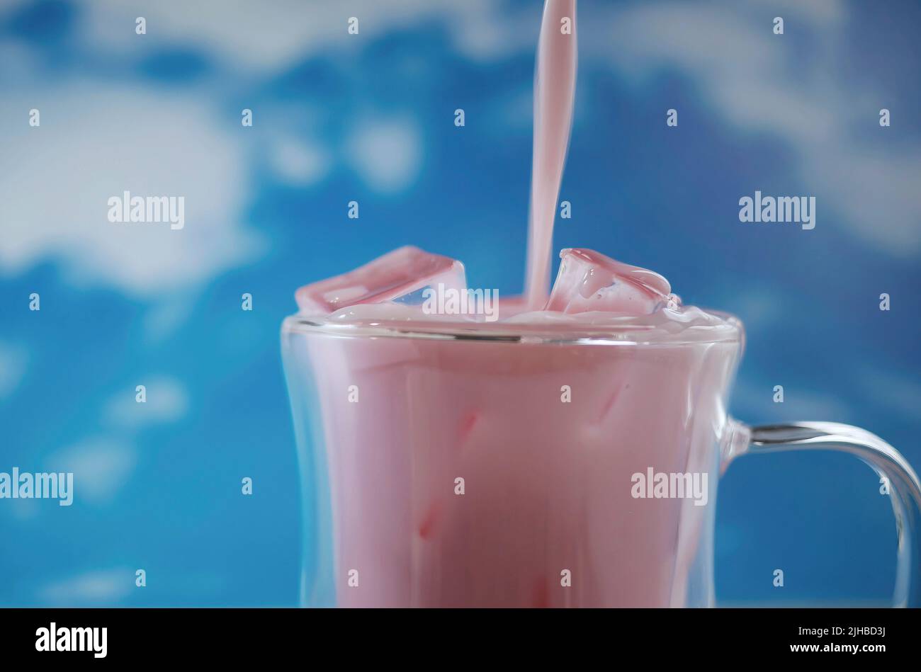 Primo piano tazza di vetro doppia con movimento versante di colore rosa pastello bevanda con sfondo cielo blu, tema pastello, movimento sfocato Foto Stock