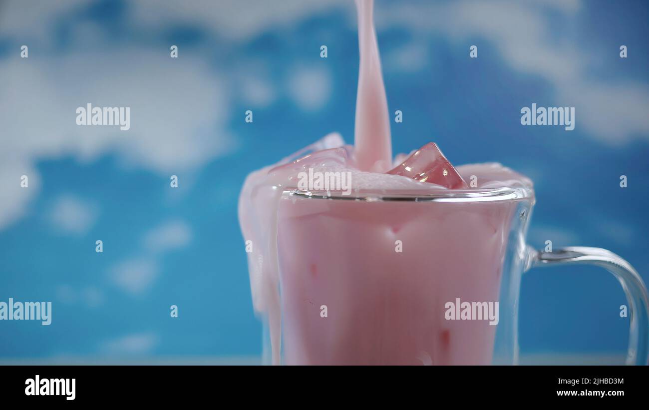 Primo piano tazza di vetro doppia con movimento versante di colore rosa pastello bevanda con sfondo cielo blu, tema pastello, movimento sfocato Foto Stock