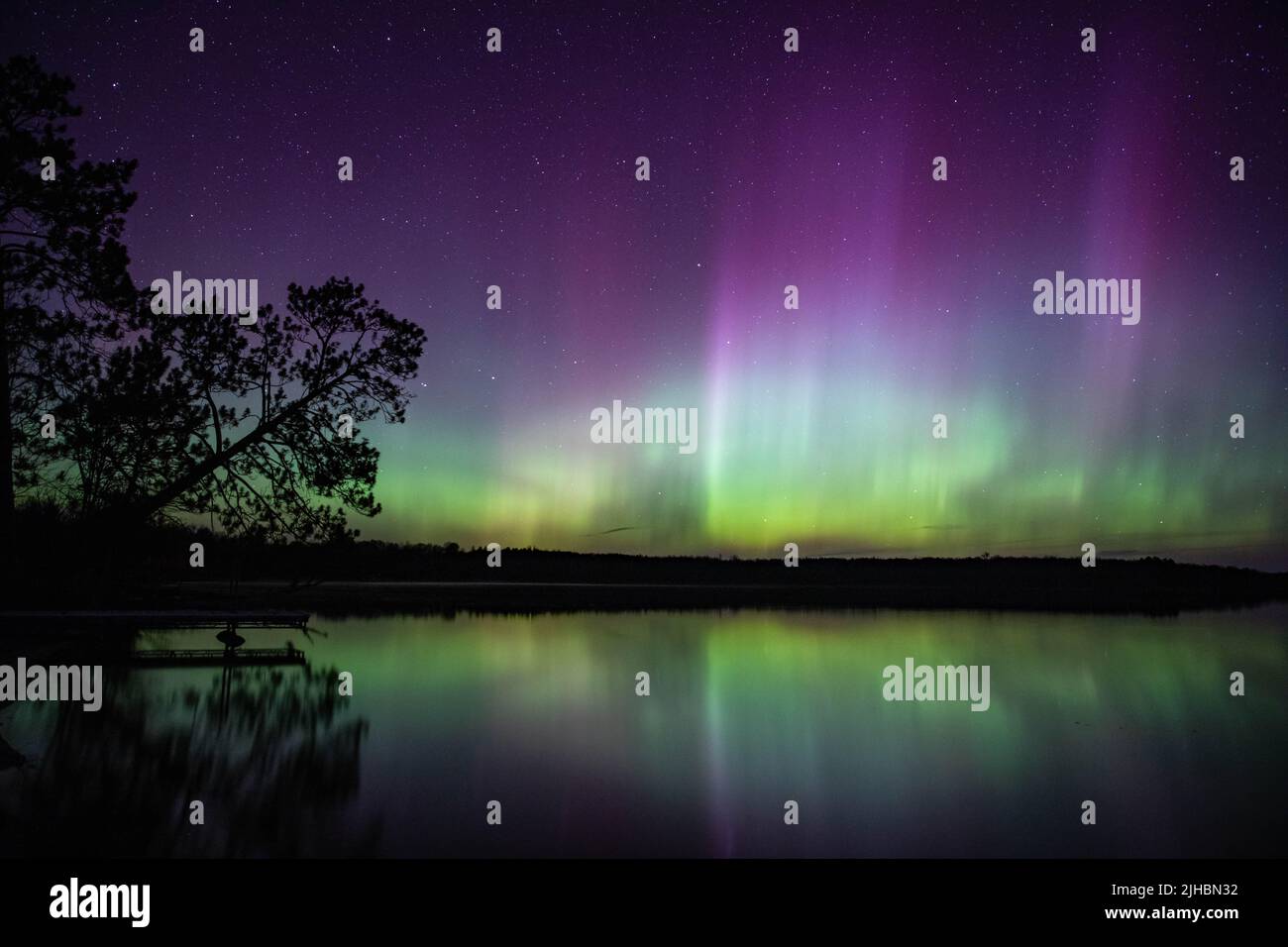 L'aurora boreale erutta su un lago del Minnesota nel cielo scuro che splende un arcobaleno di luce e colori Foto Stock