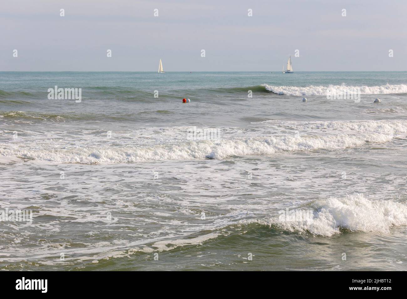 L'estate vibes sulla soleggiata spiaggia autunnale di Malvarrosa a Valencia, Spagna. Barche a vela in mare galleggiante lungo le ondate spumeggianti. Foto Stock