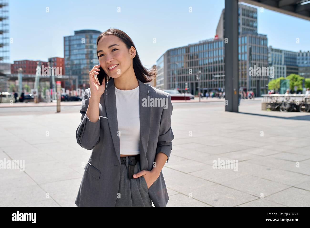 La giovane donna asiatica d'affari indossa il vestito in piedi sulla strada della città parlando al telefono. Foto Stock