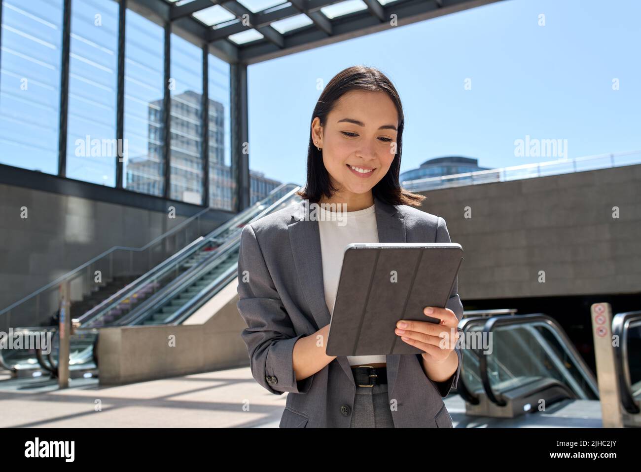 Sorridente giovane donna asiatica d'affari in piedi nella metropolitana della città usando il tablet. Foto Stock