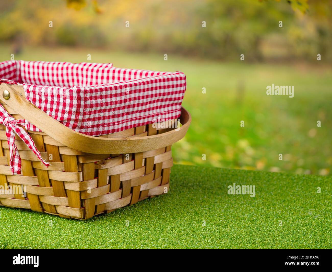 Vacanze estive, picnic all'aperto. Su un prato verde, un carino cestino da picnic con paglia sullo sfondo della natura estiva. Tradizioni familiari, romanticismo, holida Foto Stock
