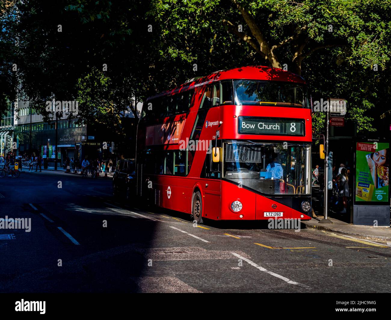 Il Red London Bus emerge dalle ombre nel centro di Londra. Un autobus New Routemaster n. 8 per Bow Church è parcheggiato in parte all'ombra in una strada londinese. Foto Stock