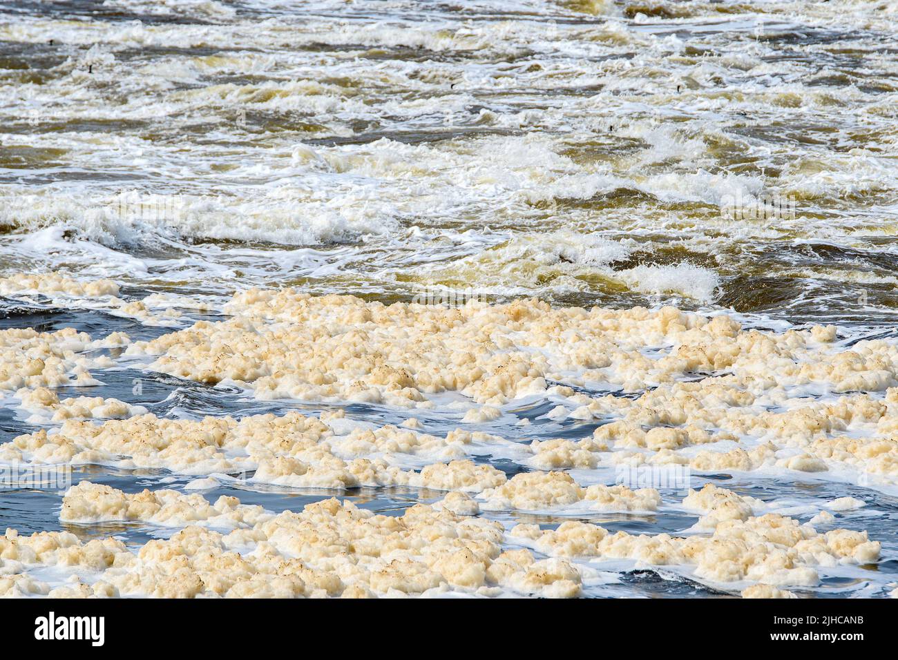 Un fiume che scorre velocemente riempito di schiuma inquinante sporca. La schiuma è di colore marrone chiaro e sporco. Profondità di campo poco profonda. Foto Stock