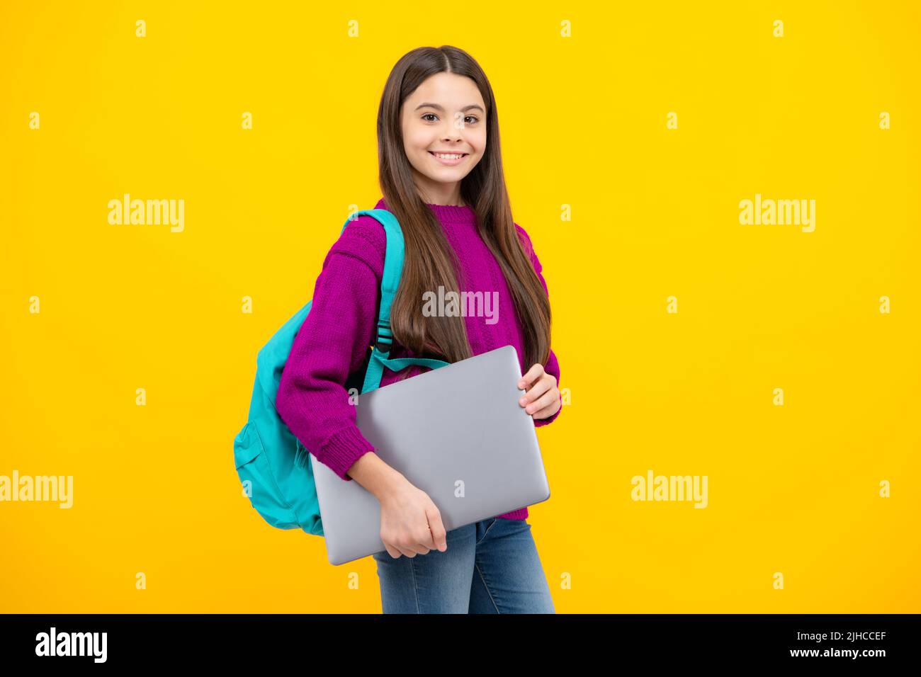 Schoolchild, studentessa adolescente con computer portatile su sfondo giallo isolato studio. Scuola per bambini e concetto di istruzione. Foto Stock