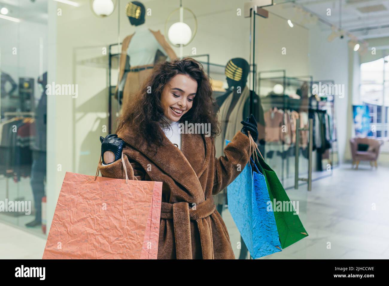 Vendita vacanze. Bella giovane donna ricci in pelliccia cappotto che tiene carta borse colorate con shopping e regali per le vacanze di Natale per la famiglia e gli amici. Spettacoli, brags, gioie, guarda la macchina fotografica in un negozio in un centro commerciale Foto Stock