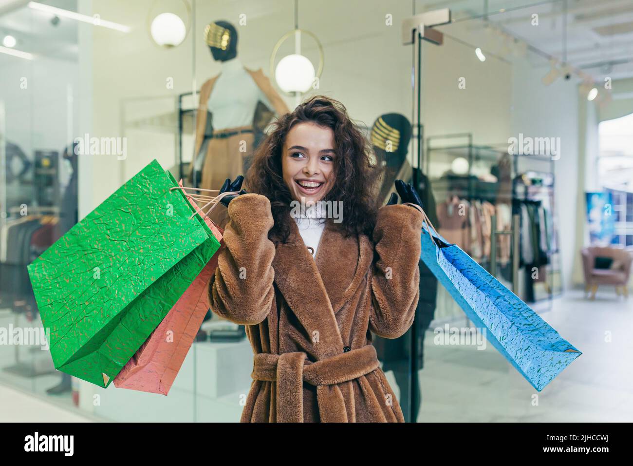 Vendita vacanze. Bella giovane donna ricci in pelliccia cappotto che tiene carta borse colorate con shopping e regali per le vacanze di Natale per la famiglia e gli amici. Spettacoli, brags, gioie, guarda la macchina fotografica in un negozio in un centro commerciale Foto Stock
