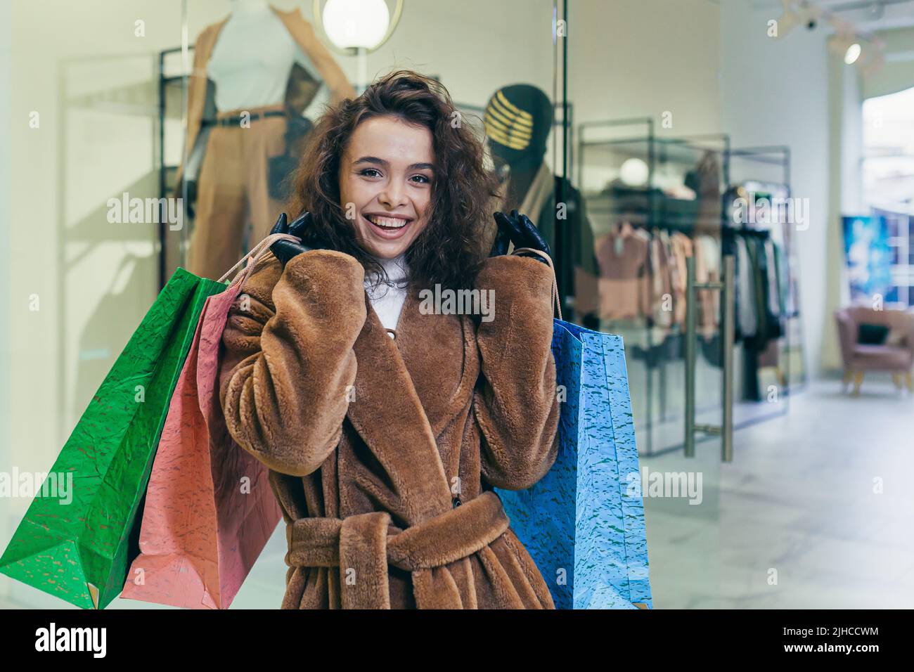 Vendita vacanze. Bella giovane donna ricci in pelliccia cappotto che tiene carta borse colorate con shopping e regali per le vacanze di Natale per la famiglia e gli amici. Spettacoli, brags, gioie, guarda la macchina fotografica in un negozio in un centro commerciale Foto Stock