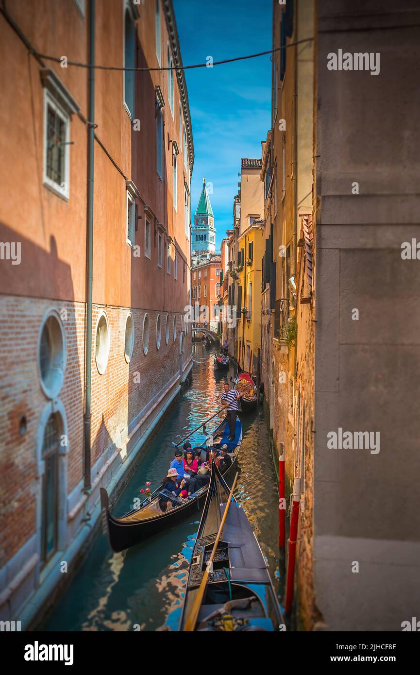 Una Gondoliere che guida gli ospiti sulla sua Gondola attraverso un piccolo canale di Venezia, Italia con il Campanile di San Giorgio maggiore sullo sfondo Foto Stock