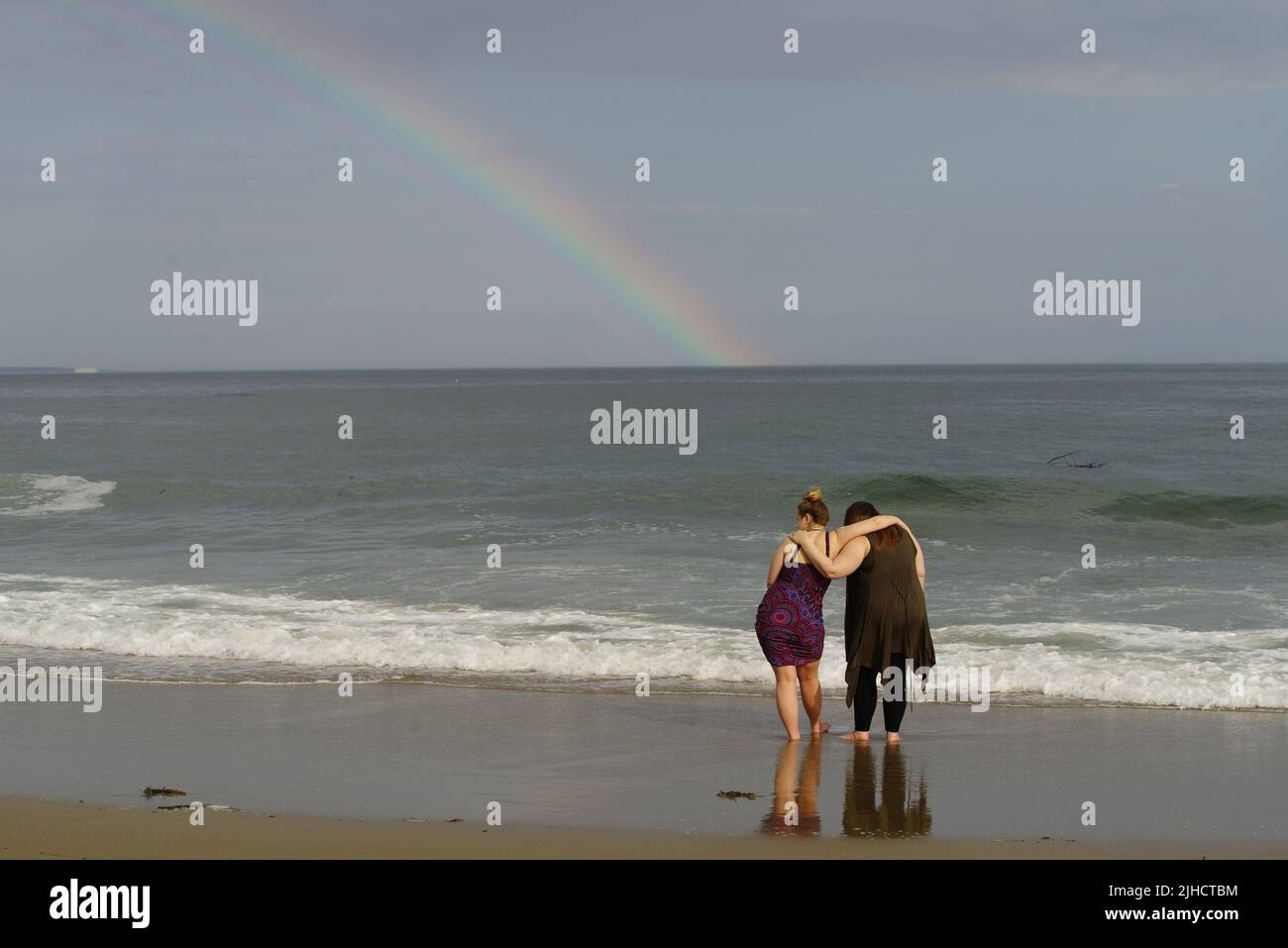 Due donne abbracciano mentre osservano una forma arcobaleno sulle acque del Golfo del Maine. Foto Stock