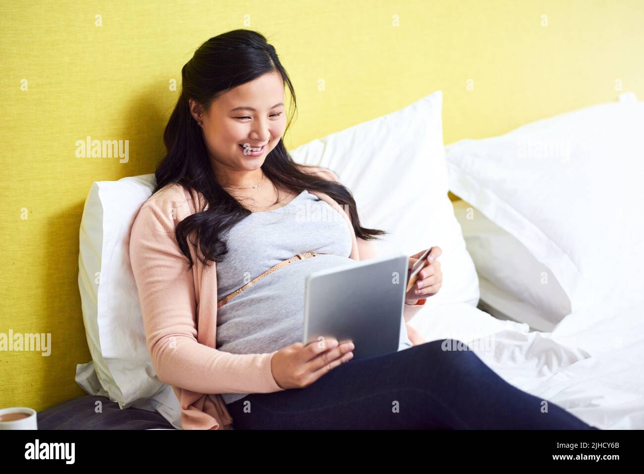 Fai scorta di articoli essenziali per il tuo bambino acquistando online. Una donna incinta che usa un tablet digitale e una carta di credito a casa. Foto Stock