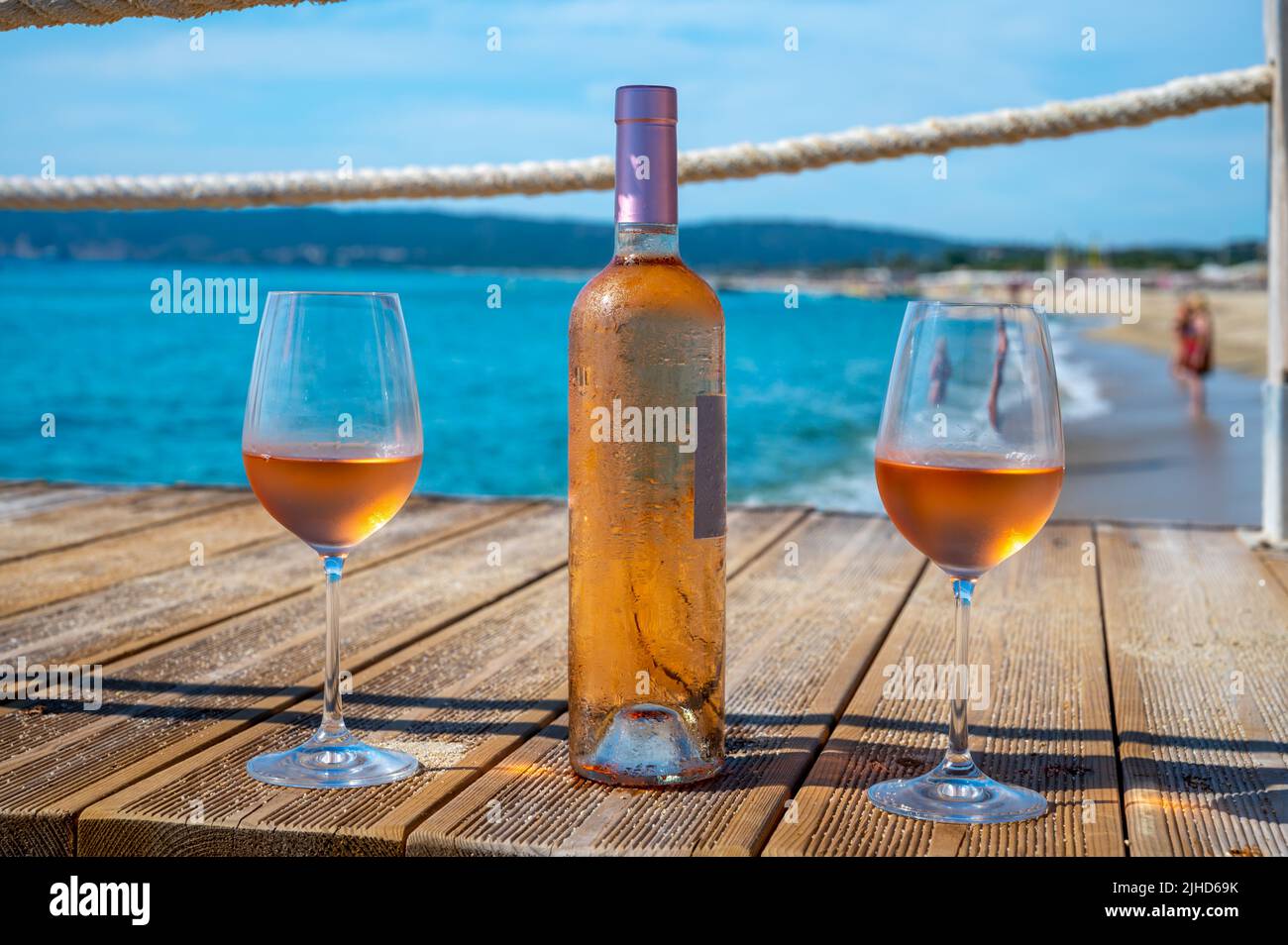 Bicchieri e bottiglia di vino rosato freddo dalla Provenza serviti all'aperto sul molo di yacht in legno con vista sull'acqua blu e la spiaggia di sabbia bianca Plage de Pampelon Foto Stock