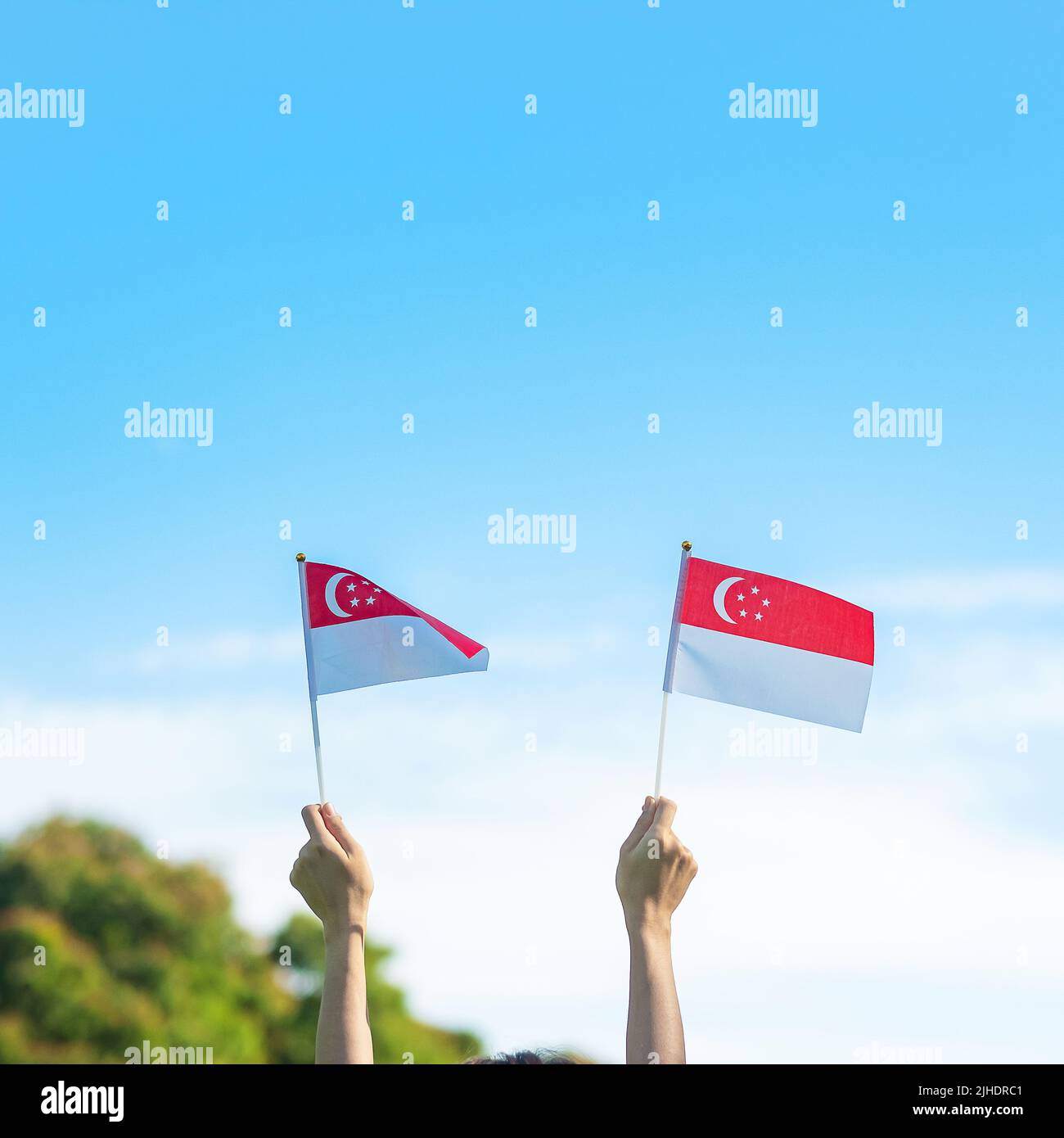 Mano che tiene la bandiera di Singapore su sfondo blu cielo. Singapore National Day e buone celebrazioni Foto Stock