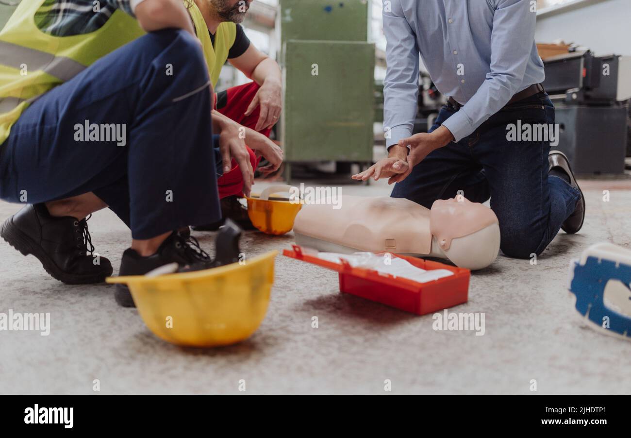 Istruttore maschile che mostra il primo soccorso medico sulla bambola durante il corso di formazione al chiuso Foto Stock