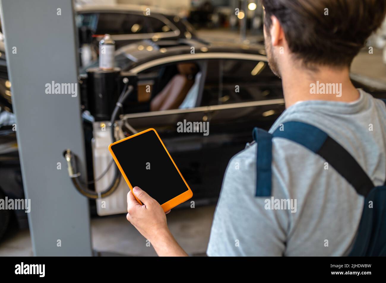 Meccanico con tablet di nuovo alla fotocamera guardando l'auto Foto Stock