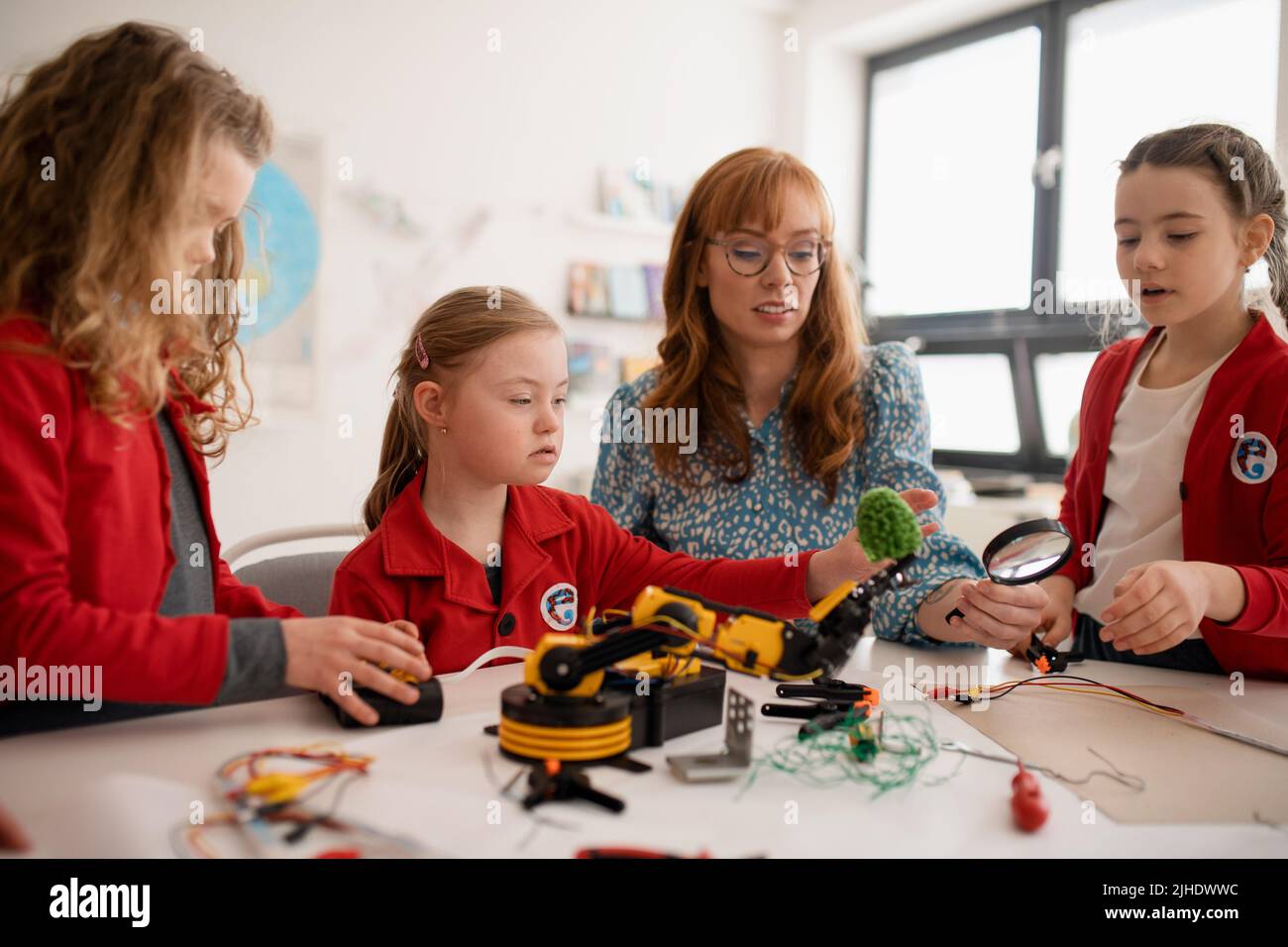 Gruppo di bambini con insegnante di scienze giovani che programmano giocattoli elettrici e robot in aula di robotica Foto Stock