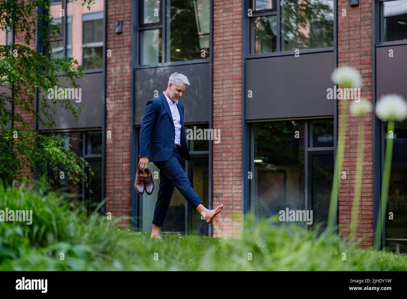 Uomo d'affari camminando a piedi nudi nel parco, sentendosi libero, concetto di equilibrio di vita di lavoro. Foto Stock